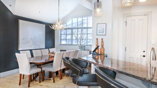 A modern kitchen with a dining area, featuring a large window, a chandelier, and a white door. - Charlie's Slopeside: Ski-In/Out Penthouse, Sleeps 12, 3,040 Sq Ft, AC, BC Village, Walk Everywhere (Beaver Creek)