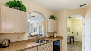 A kitchen with light wooden cabinets, a double sink, and a dishwasher. There are plants on the cabinets and a coffee maker on the counter.