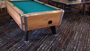 A pool table in a room with green walls and a patterned carpet.
