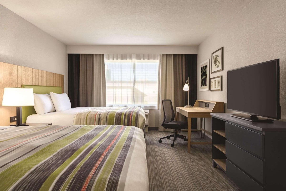 A hotel room with two beds, a desk, a chair, a television, and artwork on the wall.