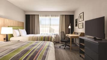 A hotel room with two beds, a desk, a chair, a television, and artwork on the wall.