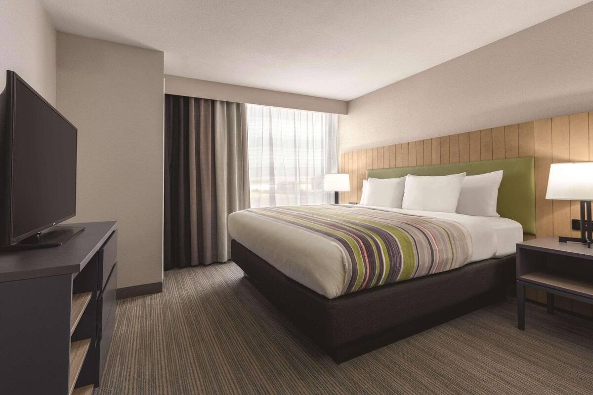 A hotel room with a large bed, a television on a desk, and a window with curtains.