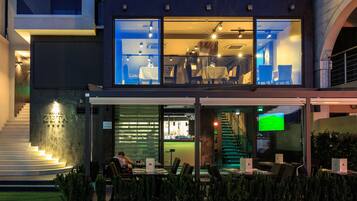 Un hotel moderno con fachada de vidrio, asientos al aire libre y una escalera que conduce a la entrada.