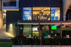 Un hotel moderno con fachada de vidrio, asientos al aire libre y una escalera que conduce a la entrada.