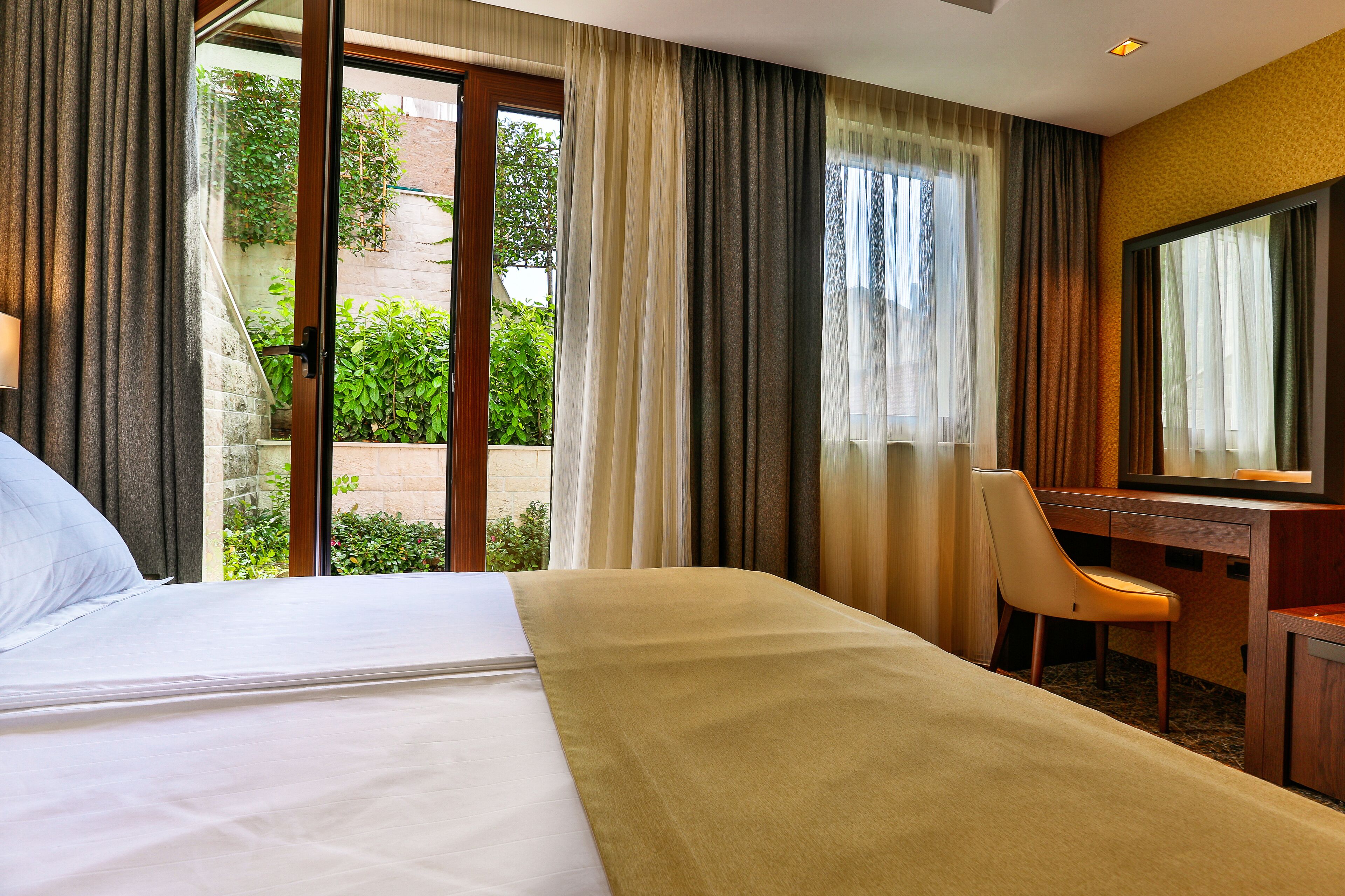 A hotel room with a bed, a desk, a chair, and a large window with curtains.