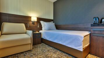 A hotel room with a bed, a chair, a nightstand, and a lamp.