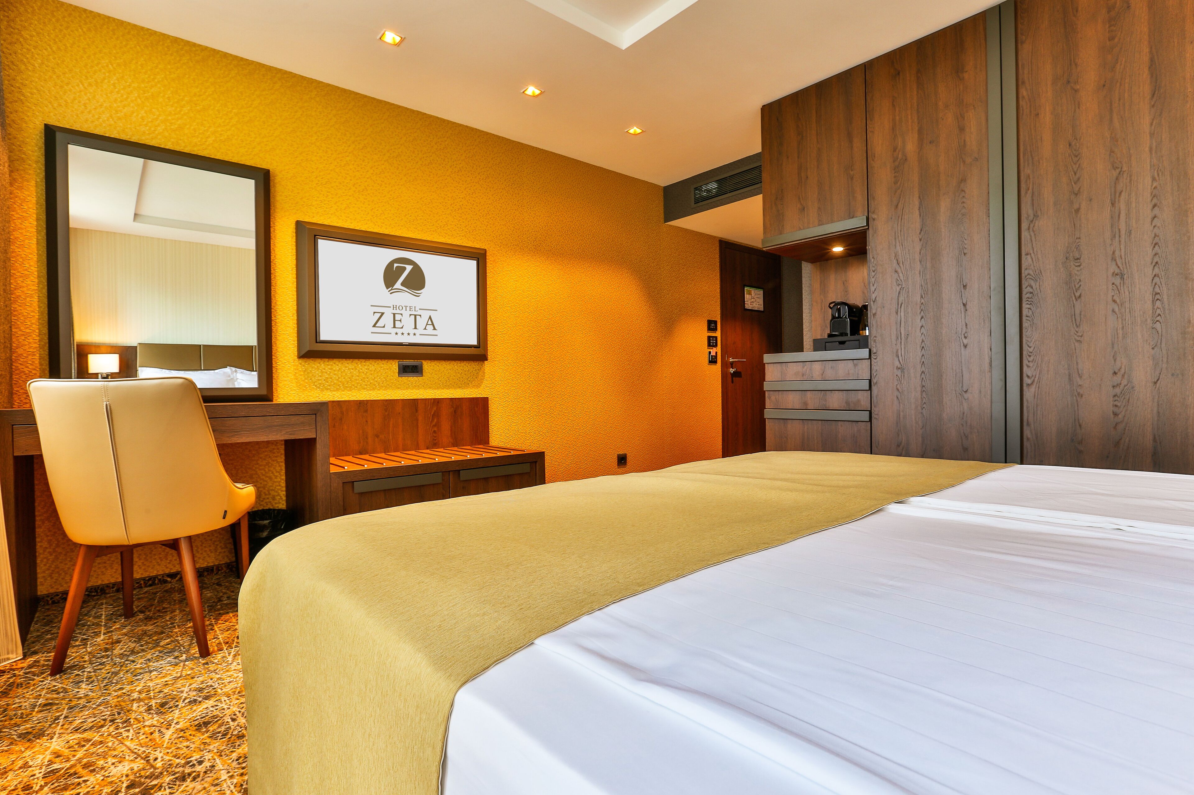 A hotel room with a large bed, a desk with a chair, a mirror, and a wooden wardrobe.