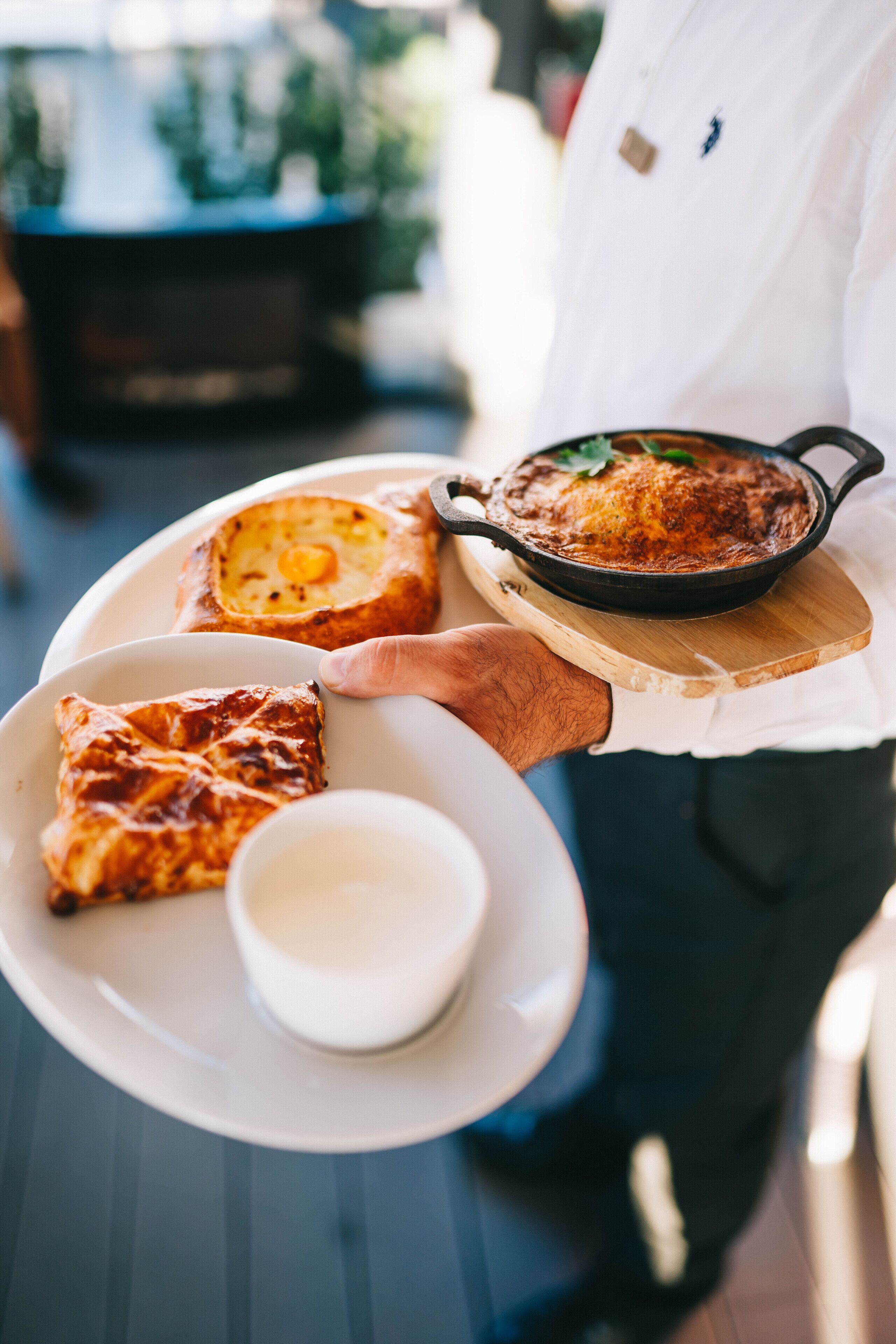 A person holding a plate with a dish and two pieces of bread, and a small cup.