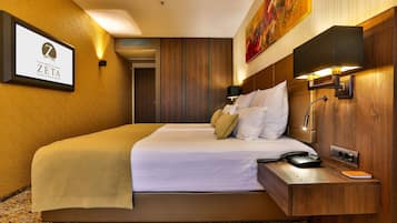 Habitación de hotel con una cama grande, una mesita de noche con lámpara, un cuadro en la pared y un cartel con el nombre del hotel.