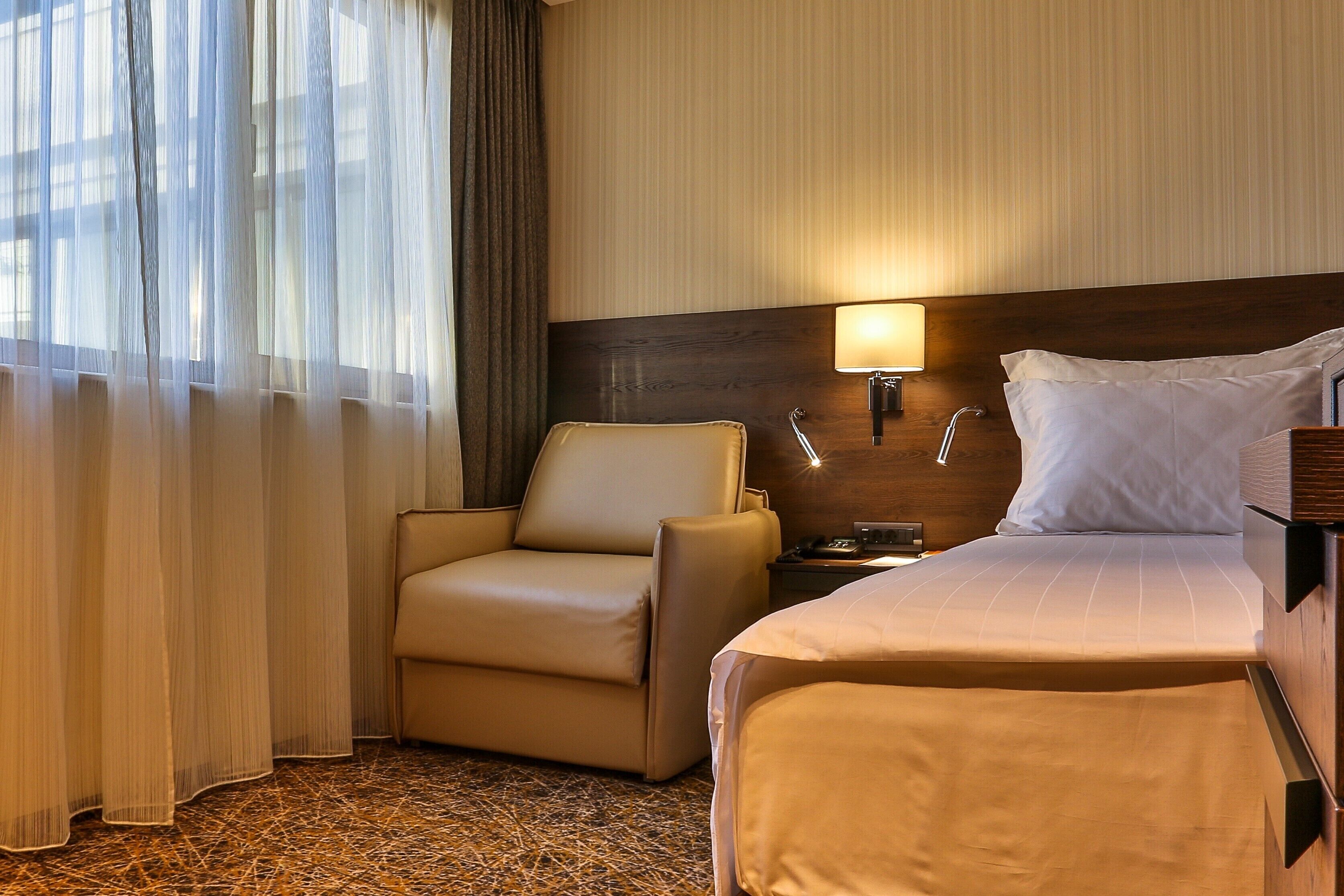 A hotel room with a bed, a chair, a nightstand, and a lamp.