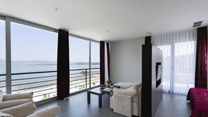 Quarto de hotel moderno com uma varanda grande, um sofá, uma poltrona e uma televisão.