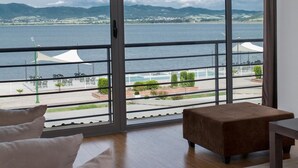 Uma sala de estar moderna com uma grande porta de vidro deslizante que dá para uma varanda com vista para um corpo de água e montanhas.