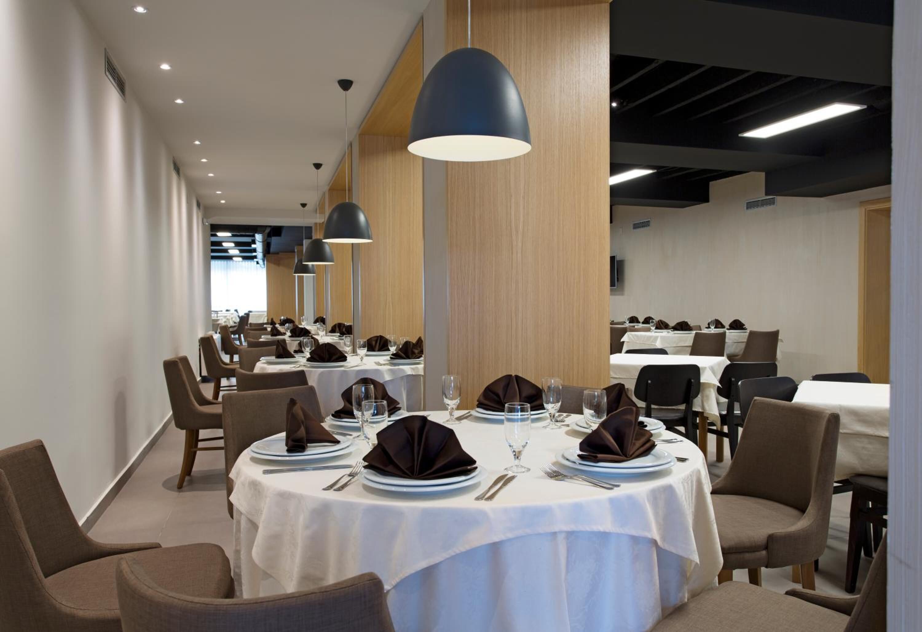 A dining area with round tables set with white tablecloths, brown napkins, and cutlery.