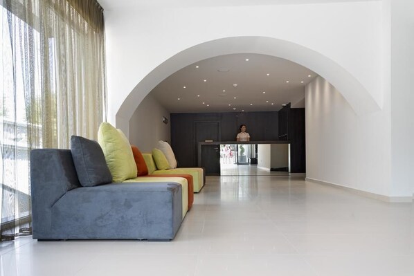 Una sala de estar moderna con un sofá, una cocina al fondo y un ventanal con cortinas.