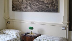 Ein Schlafzimmer mit zwei Betten, einem Nachttisch, einer grünen Lampe und einem großen historischen Gemälde an der Wand.