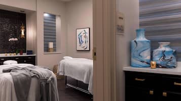 A modern spa room with two treatment beds, a large blue vase, and a framed abstract painting on the wall.