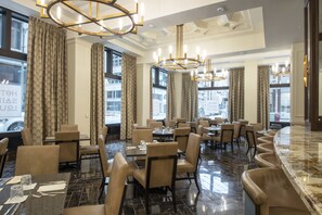 A spacious restaurant with high ceilings, chandeliers, and large windows offering city views. - Hotel Saint Louis, Autograph Collection (St. Louis)