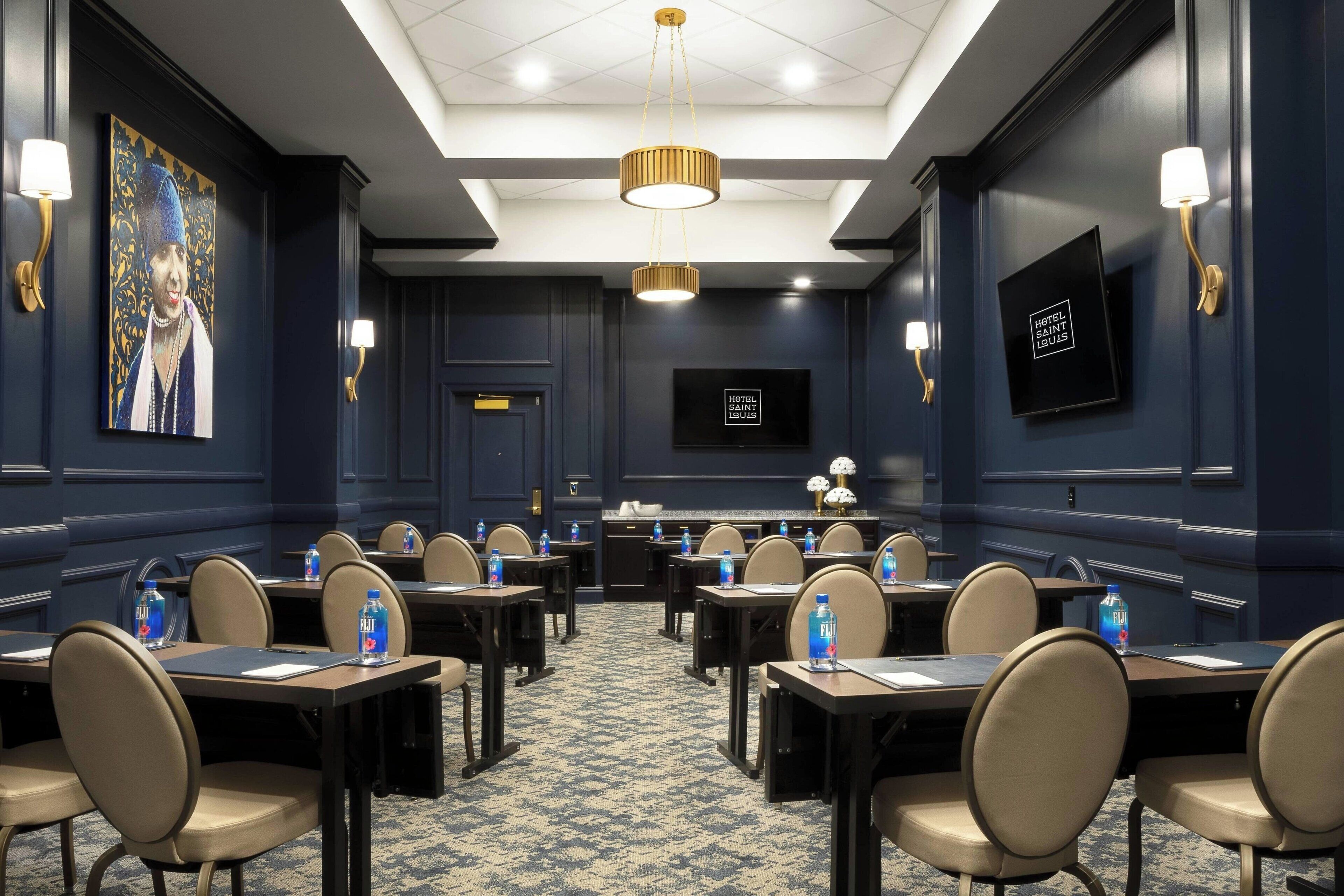 A conference room with tables, chairs, a television, and wall-mounted lamps.