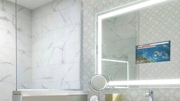 Un baño con pared de azulejos de mármol, un espejo grande con luz, un lavamanos y un mueble de color azul oscuro.