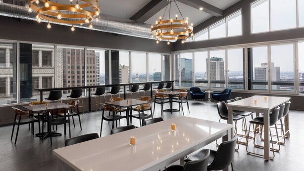 Un comedor moderno con varias mesas y sillas, ventanas amplias con vista a la ciudad, y lámparas de diseño contemporáneo.