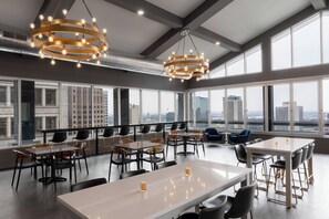A modern dining area with multiple tables and chairs, large windows with a city view, and contemporary lighting fixtures. - Hotel Saint Louis, Autograph Collection (St. Louis)