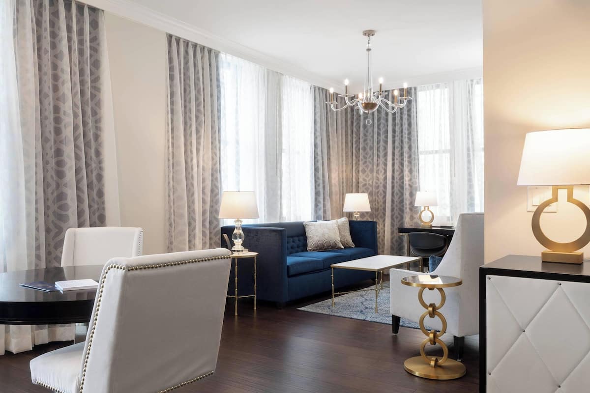 A modern living room with a blue sofa, white armchairs, a round coffee table, and a chandelier.