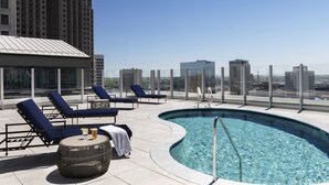 Un área de piscina en la azotea con sillones de descanso y vistas despejadas del horizonte urbano.
