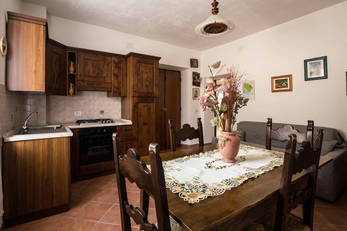 Eine Küche mit Holdekor, einem Esstisch mit Stühlen, einer Vase mit Blumen und einem grauen Sofa.