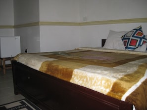 Una cama con colcha estampada, una mesita de noche y una pared blanca con interruptor de luz.