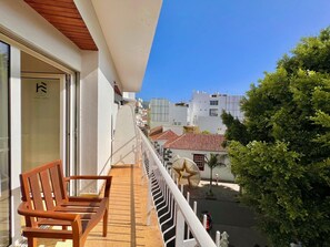 A balcony with a wooden bench, a white railing, and a view of a street with buildings and a tree. - Hotel Eden La Palma (Los Llanos de Aridane)