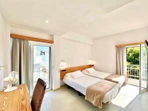 A hotel room with two beds, a desk with a fan, and a view of greenery through the windows. - Hotel Eden La Palma (Los Llanos de Aridane)