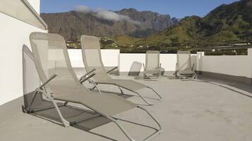 Cuatro tumbonas en una terraza en la azotea con montañas al fondo.