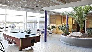 A pool table in a room with large windows, a seating area with chairs, and a planter with plants. - Danhostel Ringkøbing (Ringkobing)