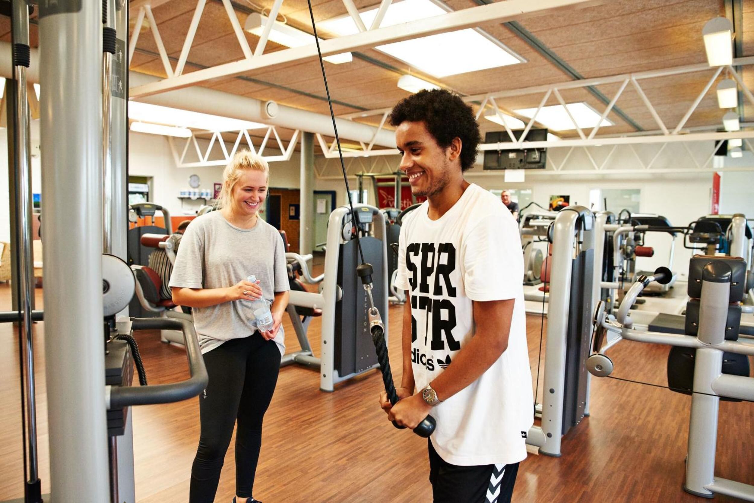 Ein Fitnessraum mit verschiedenen Trainingsgeräten, Holzboden und einer hohen Decke mit freiliegenden Balken.