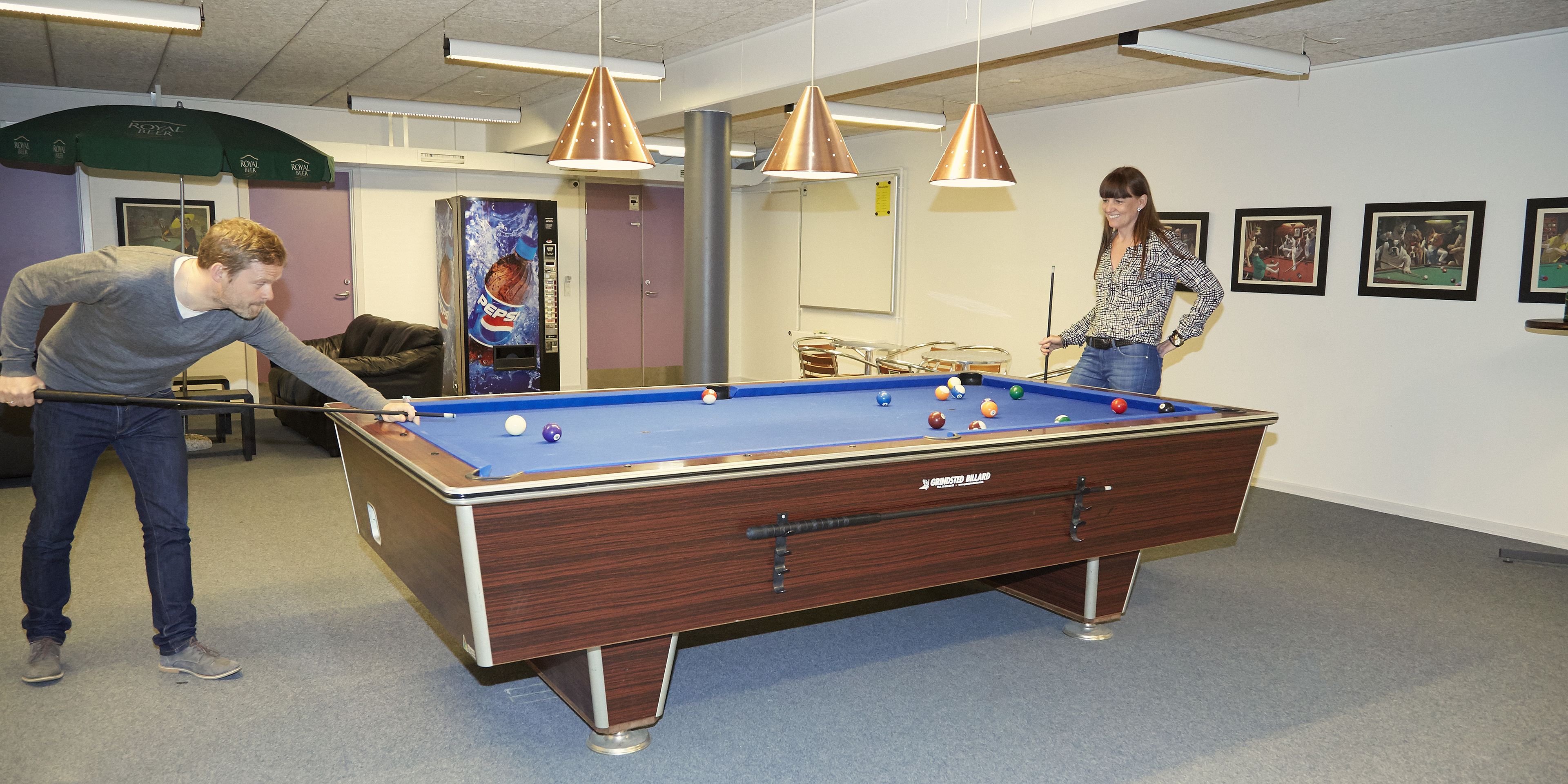 A pool table in a room with a ceiling fan, a vending machine, and framed pictures on the wall.