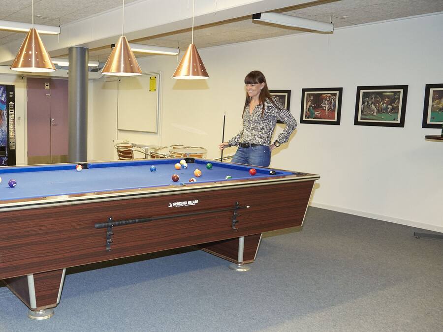 A pool table in a room with a ceiling fan, a vending machine, and framed pictures on the wall.
