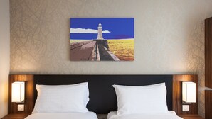 Une chambre d’hôtel avec un grand lit, deux tables de chevet avec des lampes et un tableau représentant un phare accroché au mur.
