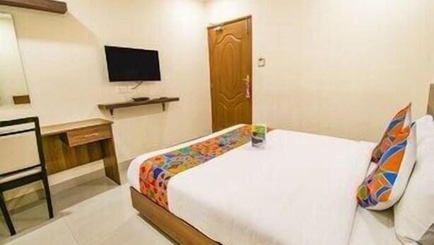 A hotel room with a bed, a desk, a television, and a door. - FabHotel Thejas Paaradise (Coimbatore)