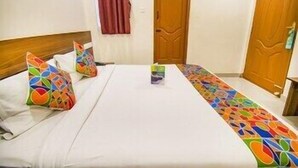 A hotel room with a bed, pillows, a nightstand, and a door. - FabHotel Thejas Paaradise (Coimbatore)