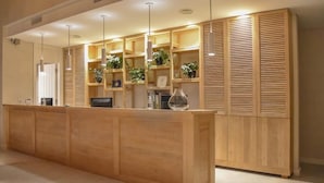 Un área de recepción con un mostrador de madera, estantes con plantas y una puerta de madera cerrada.