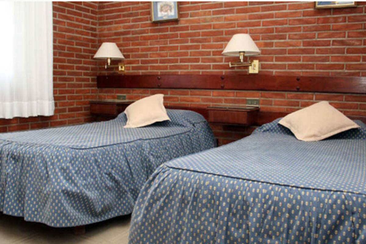 A room with two beds, a brick wall, and two wall-mounted lamps.