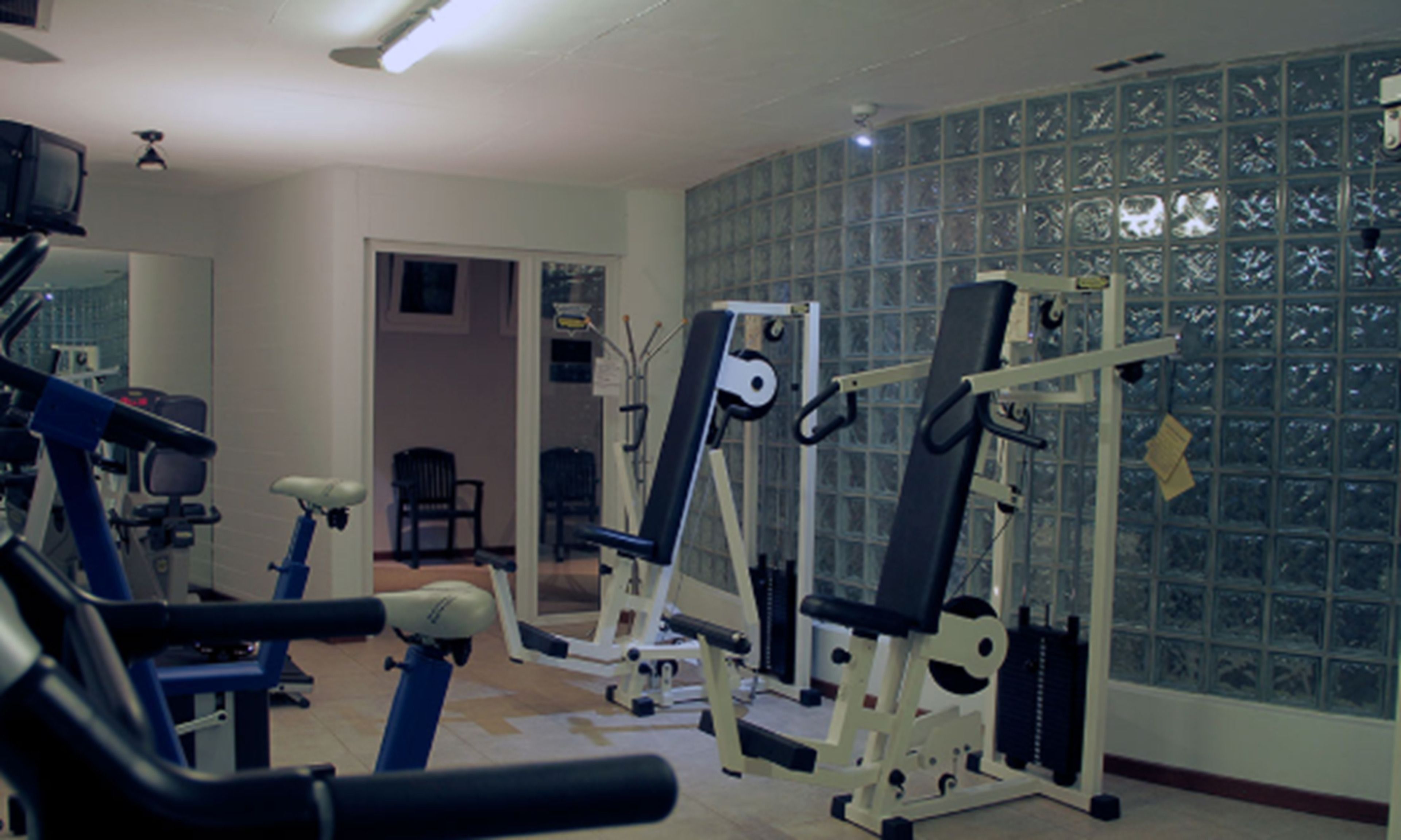 Une salle de sport équipée de matériel d’exercice, avec un miroir et une porte donnant sur une autre pièce.