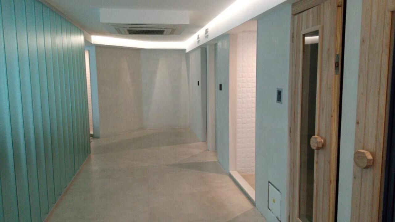 Un pasillo estrecho con paredes pintadas de color verde azulado, una puerta de madera a la derecha y un interruptor de luz en la pared.