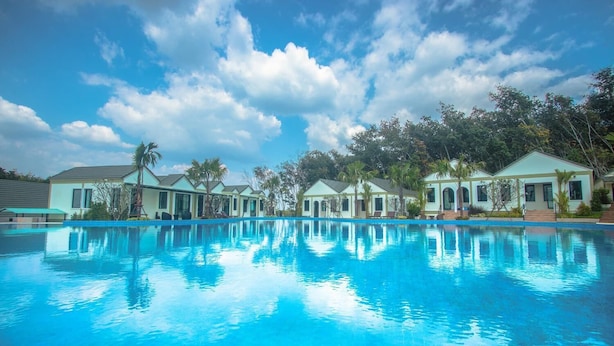 A swimming pool with a clear blue sky and clouds above. There are several buildings with a light-colored exterior and a flat roof. - Saichol Grandview (Ban Ta Khun)