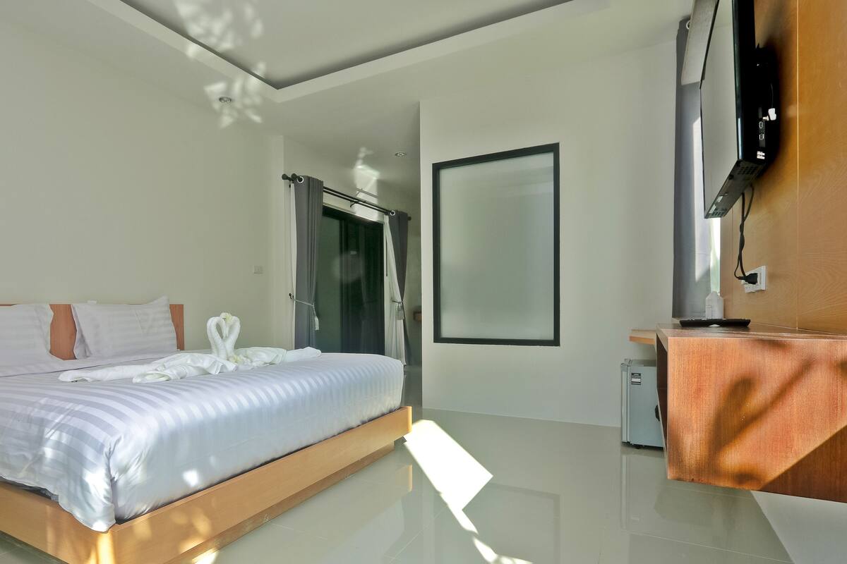 A modern hotel room with a large bed, a small desk, a TV, and a shower area.