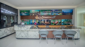 A reception area with a marble counter, three grey chairs, and a wall decorated with various travel-themed paintings. - Saichol Grandview (Ban Ta Khun)