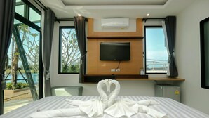 A hotel room with a bed, a TV mounted on a wooden panel, a small desk, and a view of the outdoors. - Saichol Grandview (Ban Ta Khun)