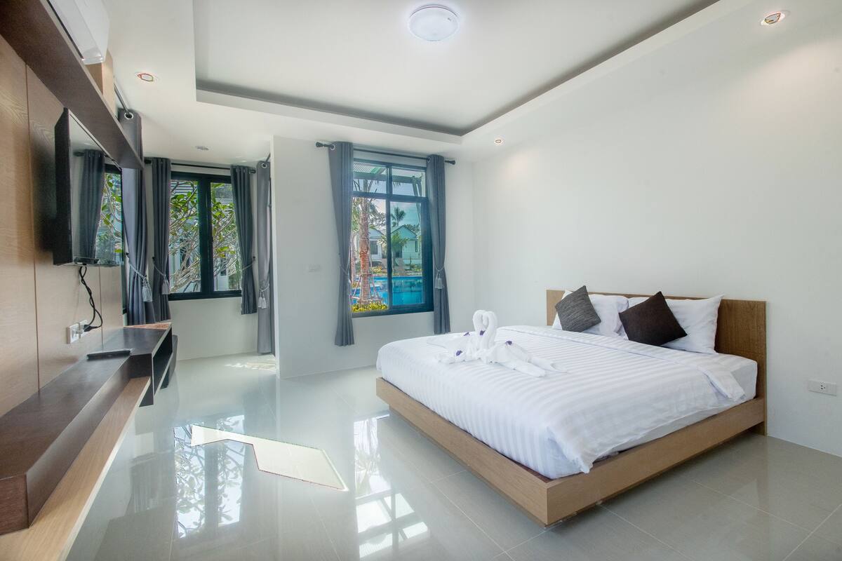 A modern bedroom with a large bed, a wooden bedside table, and a TV mounted on the wall.
