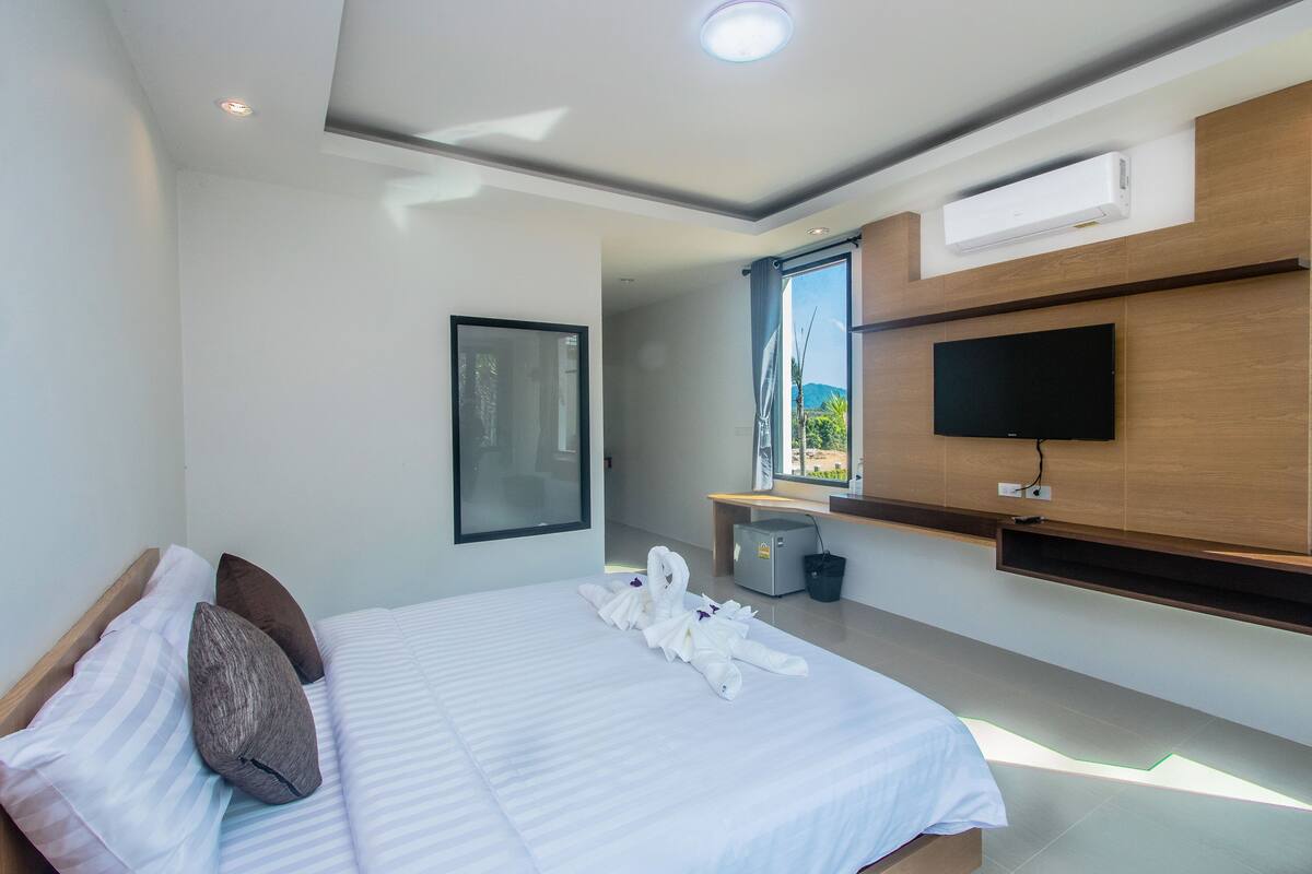 A modern hotel room with a neatly made bed, a flat-screen TV mounted on the wall, and a small desk with a chair.