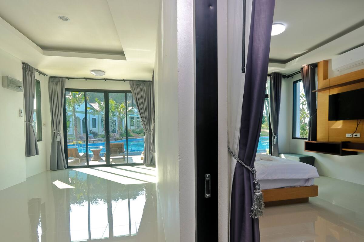 A hotel room with a large glass door leading to a pool area, a bed with a wooden headboard, and a mounted TV.